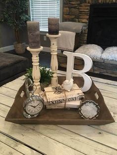 a wooden tray with candles, books and an alarm clock on it in front of a fireplace