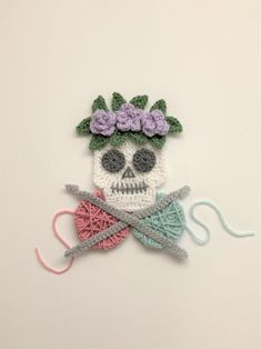 a crocheted skull with flowers on it's head holding a knitting needle