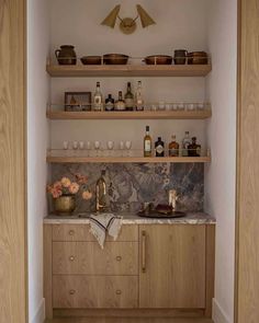 a kitchen with wooden cabinets and shelves filled with bottles on top of each shelf next to a sink