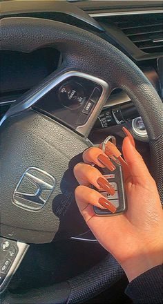 a woman driving a car with her hands on the steering wheel and nails painted orange