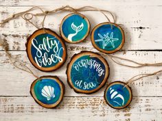 four wood slice ornaments with hand painted words and seashells on them sitting on a white wooden surface