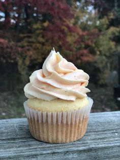 a cupcake with white frosting sitting on top of a wooden table next to trees