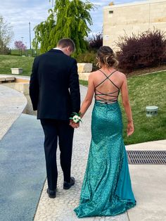 a man and woman dressed in formal wear walking down a sidewalk with one holding the other's hand