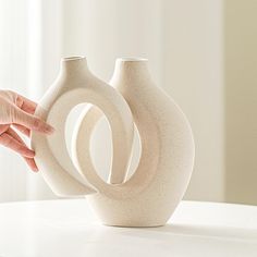 two white vases on a table with one being held up by the other hand