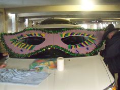 two people standing next to a car decorated with mardi gras