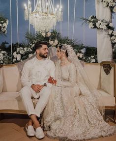 a bride and groom sitting on a couch in front of a chandelier