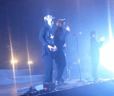 two men standing on stage with microphones in their hands and one man wearing a suit