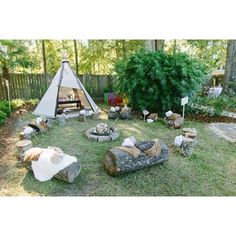 a teepee tent in the middle of a yard with logs and chairs around it