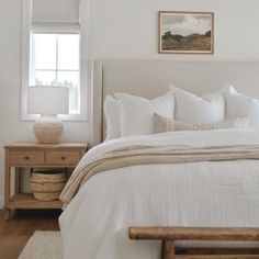 a bed with white linens and pillows in a bedroom next to a wooden table