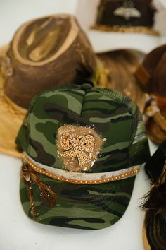 Turn heads with this one-of-a-kind GOLDEN BOW CAMO TRUCKER HAT, flaunting an adjustable snapback, striking gold beaded bow patch, luxurious fur and brown leather band, and eye-catching brown feather combo with golden glitter accents. Get that cool, edgy look today! This is a made-to-order item. All customized orders are currently shipping within 14 business days. To receive item quicker, expedited shipping is available at checkout. Camo Trucker Hat, Golden Bow, Beaded Bow, Golden Glitter, Edgy Look, Leather Band, Gold Beads, Trucker Hat, Brown Leather