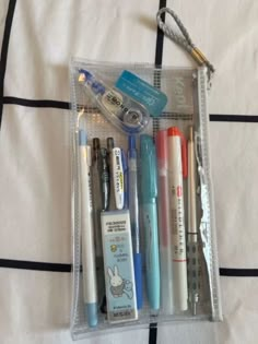 a clear case filled with lots of different types of pens and pencils on top of a bed