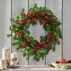 a christmas wreath with red berries and greenery on a table in front of a wooden wall