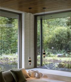 a living room filled with furniture and large windows overlooking a forest outside the window sill