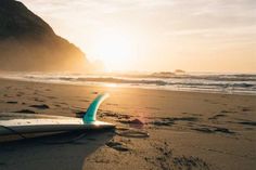 a surfboard is laying on the beach at sunset