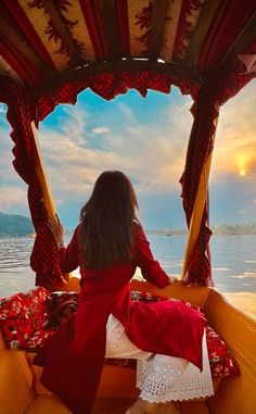 a woman sitting in the back of a boat looking out over water at sunset or sunrise