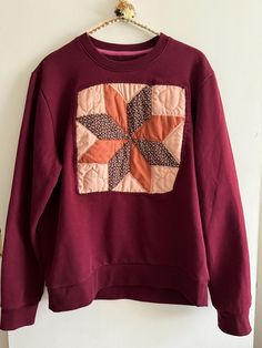 a red sweatshirt with an orange and brown patchwork design on it hanging from a hook