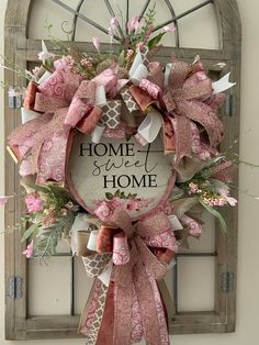 a pink and white wreath with the words home sweet home on it hanging in front of a window