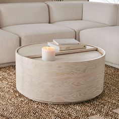 a coffee table with a candle and books on it in front of a white couch