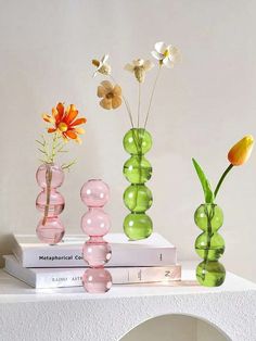 three vases with flowers in them sitting on top of books