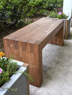 a wooden bench sitting next to two cement planters filled with flowers and greenery