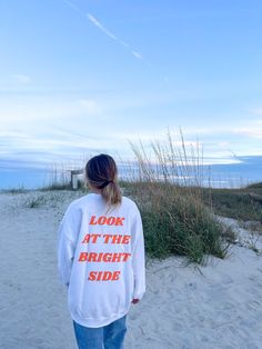 a woman standing on top of a sandy beach next to tall grass and sea oats