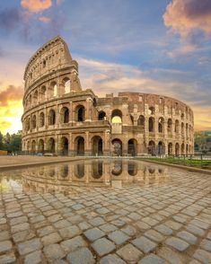 the roman colossion is reflected in water on a cobblestone surface at sunset