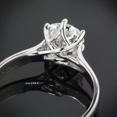 a close up view of a diamond ring on a black surface with the reflection of it's center stone