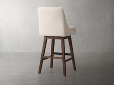 an upholstered bar stool with wooden legs and backrests, in front of a gray wall