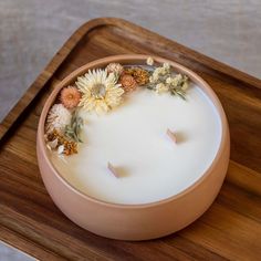 a candle with flowers floating in it on a wooden tray