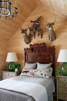 a bed room with a neatly made bed and two deer head mounted on the wall