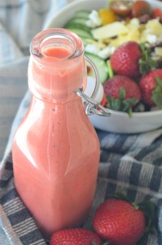 a bowl of fruit next to a bottle of smoothie with strawberries on the side