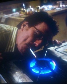 a man with glasses is leaning over a burner and looking at the blue flame