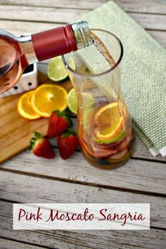 pink moscato sangria being poured into a pitcher with sliced oranges and strawberries