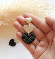 a person holding two heart shaped earrings in their hand, one is black and the other is white