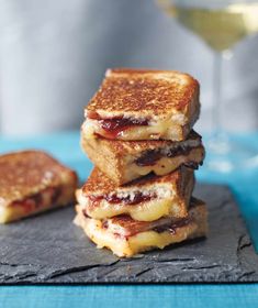 three grilled cheese sandwiches stacked on top of each other next to a glass of wine