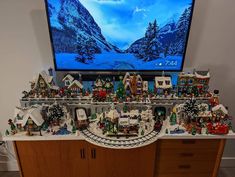 a large flat screen tv sitting on top of a wooden dresser next to a christmas village