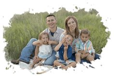 a family sitting on the ground in front of some tall grass