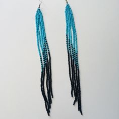 two strands of blue beads are hanging from silver earwires on a white surface