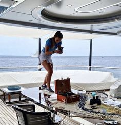 a woman standing on the deck of a boat looking at her cell phone and luggage