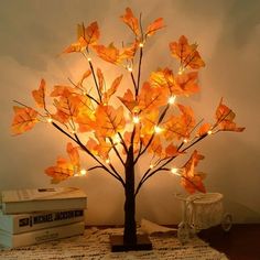 a lighted tree is sitting on a table next to some books and a vase with flowers