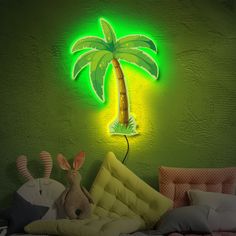 a neon green palm tree is lit up on the wall above a bed with pillows