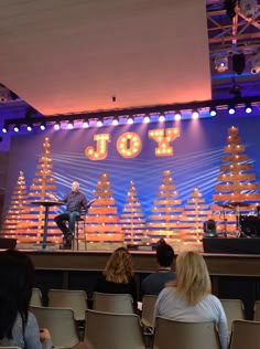 people sitting on chairs in front of a stage with the word joy written on it