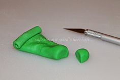 a green object next to a pen on top of a white surface with the tip of a knife sticking out of it