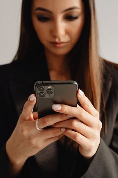 a woman is looking at her cellphone while wearing a black blazer and white nails