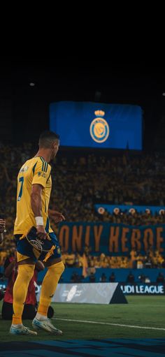 two soccer players in yellow and blue uniforms are on the field with fans behind them