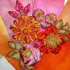 an arrangement of flowers is displayed on a table cloth with oranges and pinks