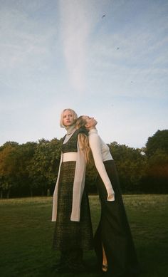 two women are standing in the grass with their arms around each other and looking into the distance