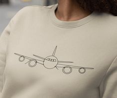 "Takeoff in style. This minimalist airplane line drawing graphic shirt is perfect for the traveler or pilot! Gift this aviation t-shirt to that special someone who travels a lot and explore everything there is to see. Soft and comfortable classic fit crewneck sweatshirt. For an oversized look size up. Size:  See product photos for size chart Material:  - Preshrunk fleece knit - Air jet yarn, softer feel and reduced pilling - Double-needle stitching at shoulder, armhole, neck, waistband, and cuffs - 1 x 1 rib with spandex - Quarter-turned to eliminate center crease - Classic fit - Tear away label Care Instructions: - Machine wash at a low heat. - Wash garments inside-out, with similar colors. - Avoid using bleach. Use non-chlorine bleach if necessary. - Do not use fabric softeners. - Tumble Airplane Shirt, Ideas Regalos, Drawing Graphic, Pilot Gifts, Airplane Mode, Cabin Crew, Cozy Fits, Travel Lover, Graphic Shirt