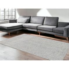 a gray couch sitting on top of a wooden floor next to a white rug and window