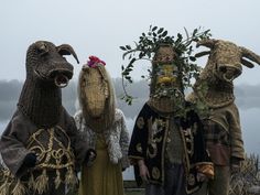 three people wearing animal masks standing next to each other in front of a body of water